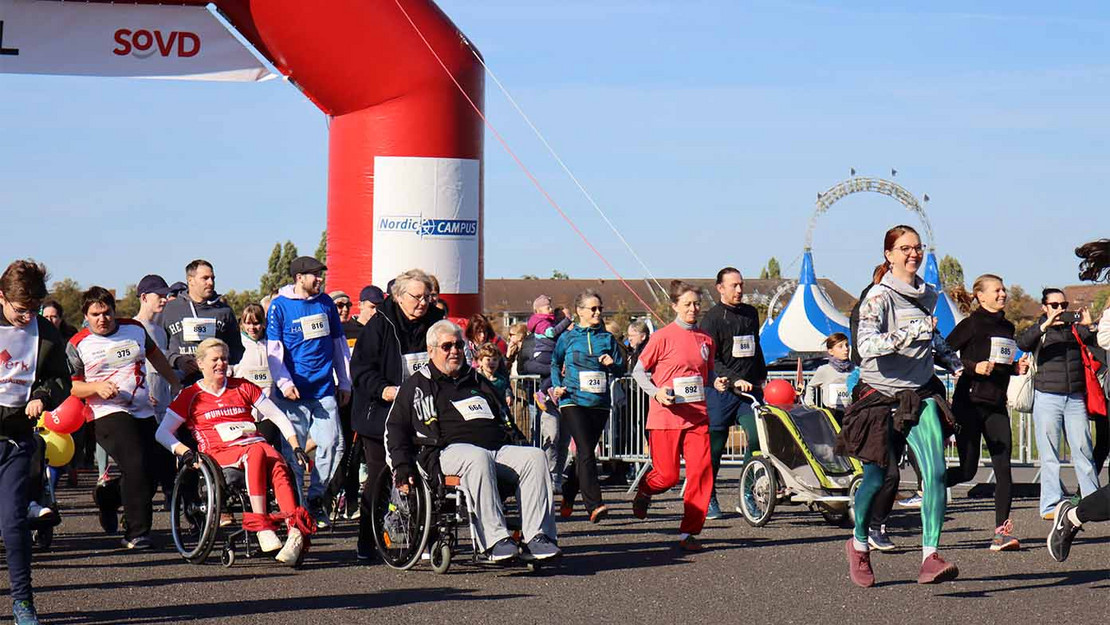 Menschen mit und ohne Rollstuhl bewewgen sich auf einer Asphaltfläche. 