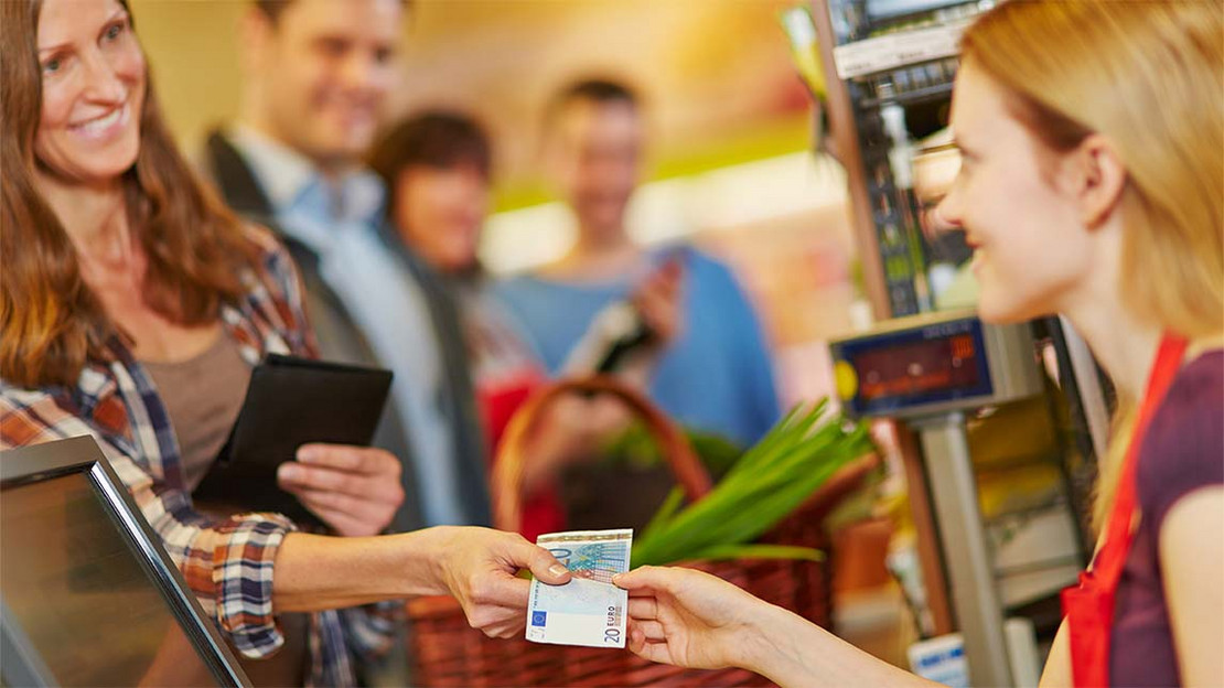 Frau reicht einer Kassiererin einen 20-Euro-Schein. 