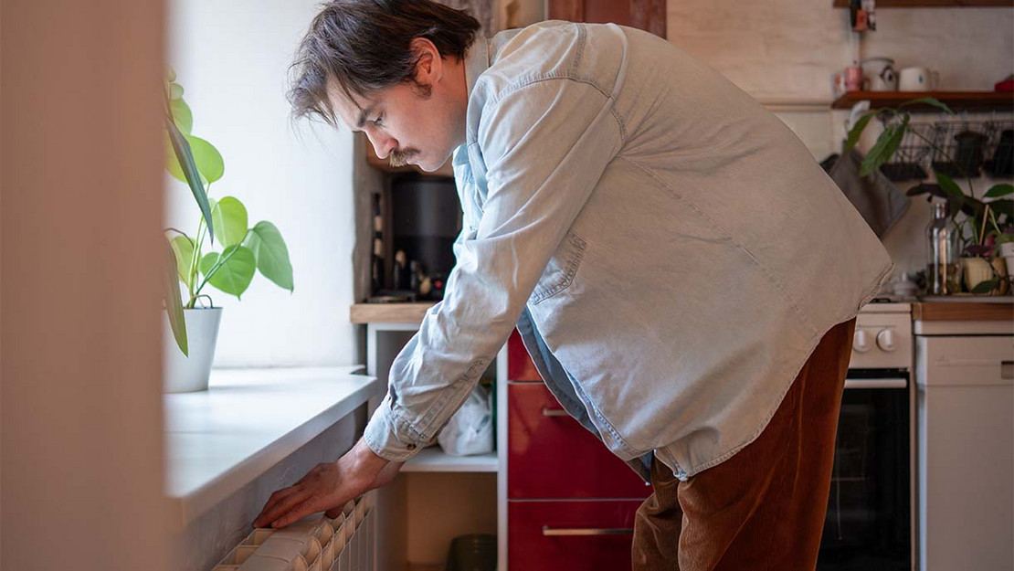Ein Mann in einer Wohnung lehnt sich auf einen Heizkörper. 