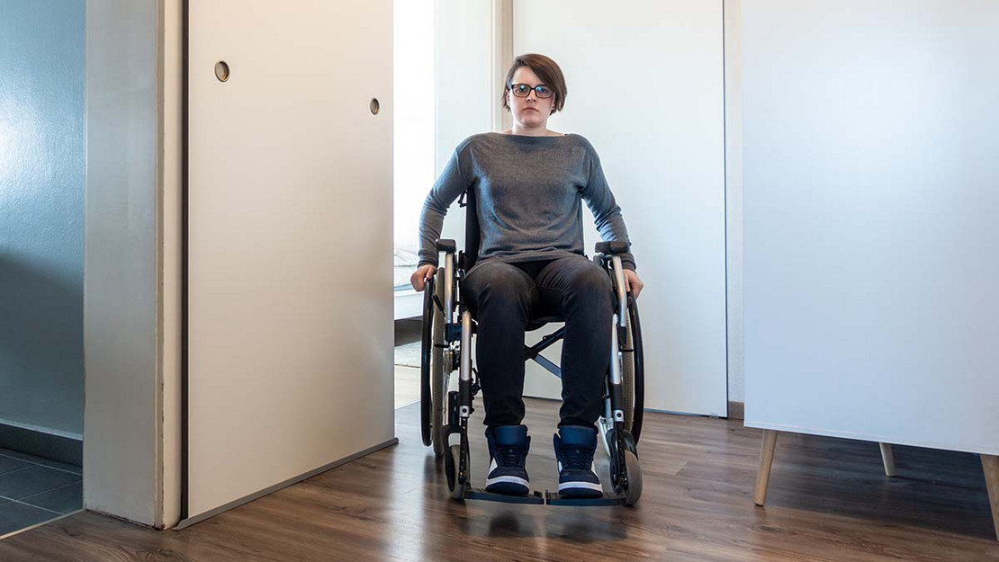 Frau im Rollstuhl auf dem Flur einer Wohnung. 