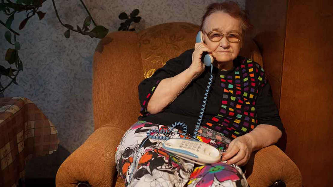 Alte Frau sitzt mit Telefonhörer im Sessel. 