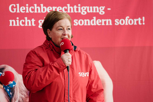 Frau steht vor einem Transparent "Gleichberechtigung - nicht gleich sondern sofort!"