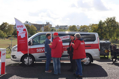 Drei Personen stehen vor einem Van mit SoVD-Aufdruck. 