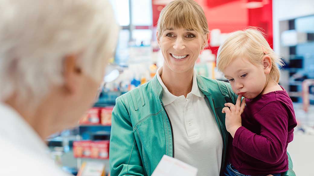 Mutter mit Kind auf dem Arm gibt ein Rezept in der Apotheke ab. 