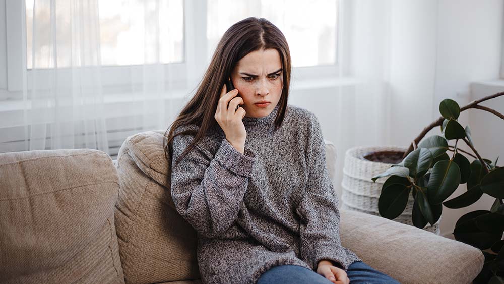 Frau mit Handy am Ohr blickt genervt. 